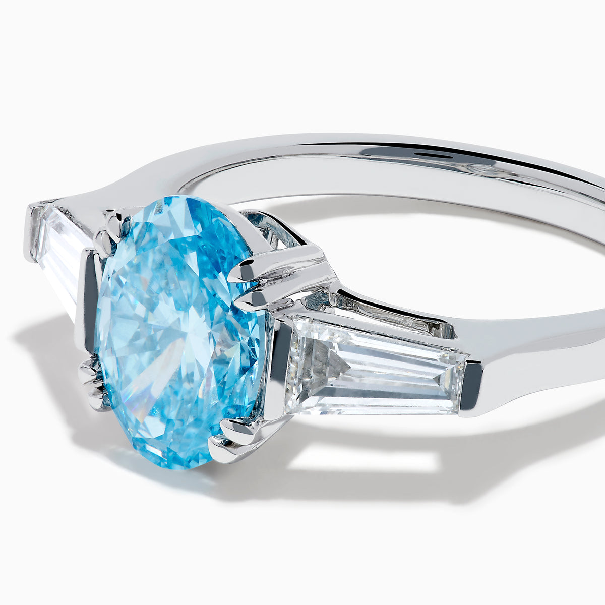 The Lab Grown Blue and White Diamond 3-Stone Ring in 14K White Gold showcases an oval blue diamond flanked by tapered white baguette diamonds, all set against a plain white background.