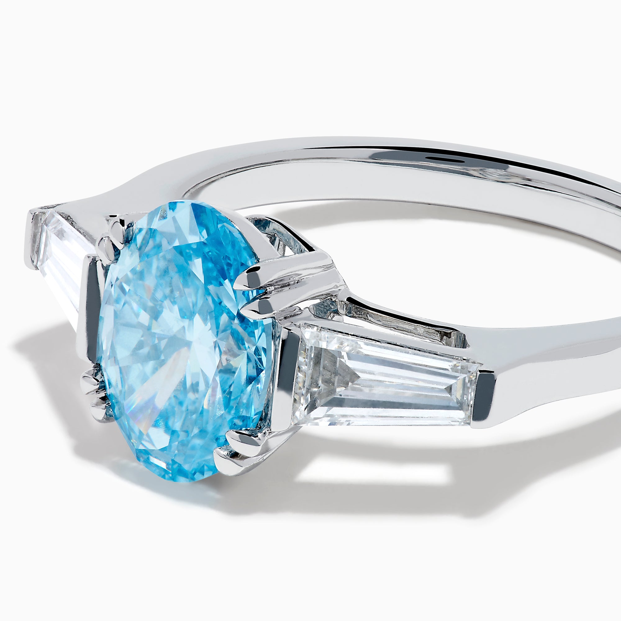 The Lab Grown Blue and White Diamond 3-Stone Ring in 14K White Gold showcases an oval blue diamond flanked by tapered white baguette diamonds, all set against a plain white background.
