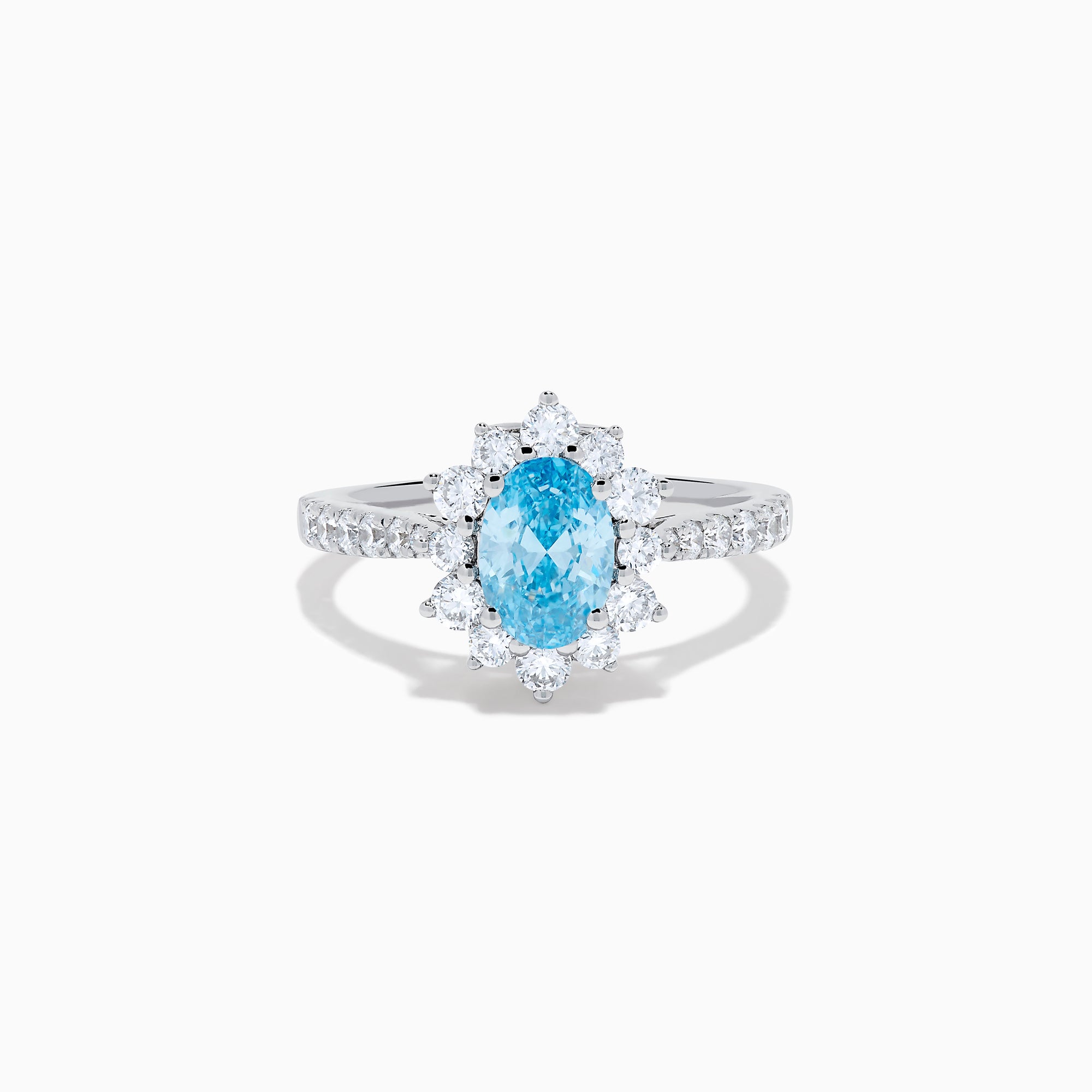 The Lab Grown Blue and White Diamond Halo Ring in 14K White Gold features an oval blue gemstone surrounded by lab grown diamonds, with more diamonds set along the band, shown on a white background.