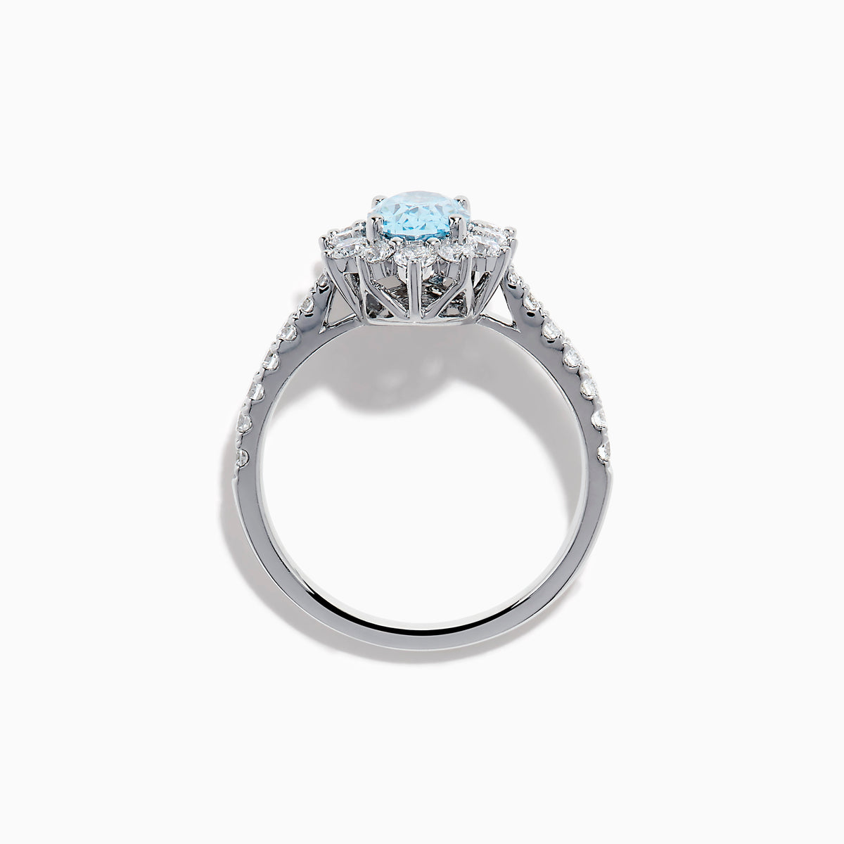 The Lab Grown Blue and White Diamond Halo Ring in 14K White Gold features an oval blue gemstone surrounded by lab grown diamonds, with more diamonds set along the band, shown on a white background.