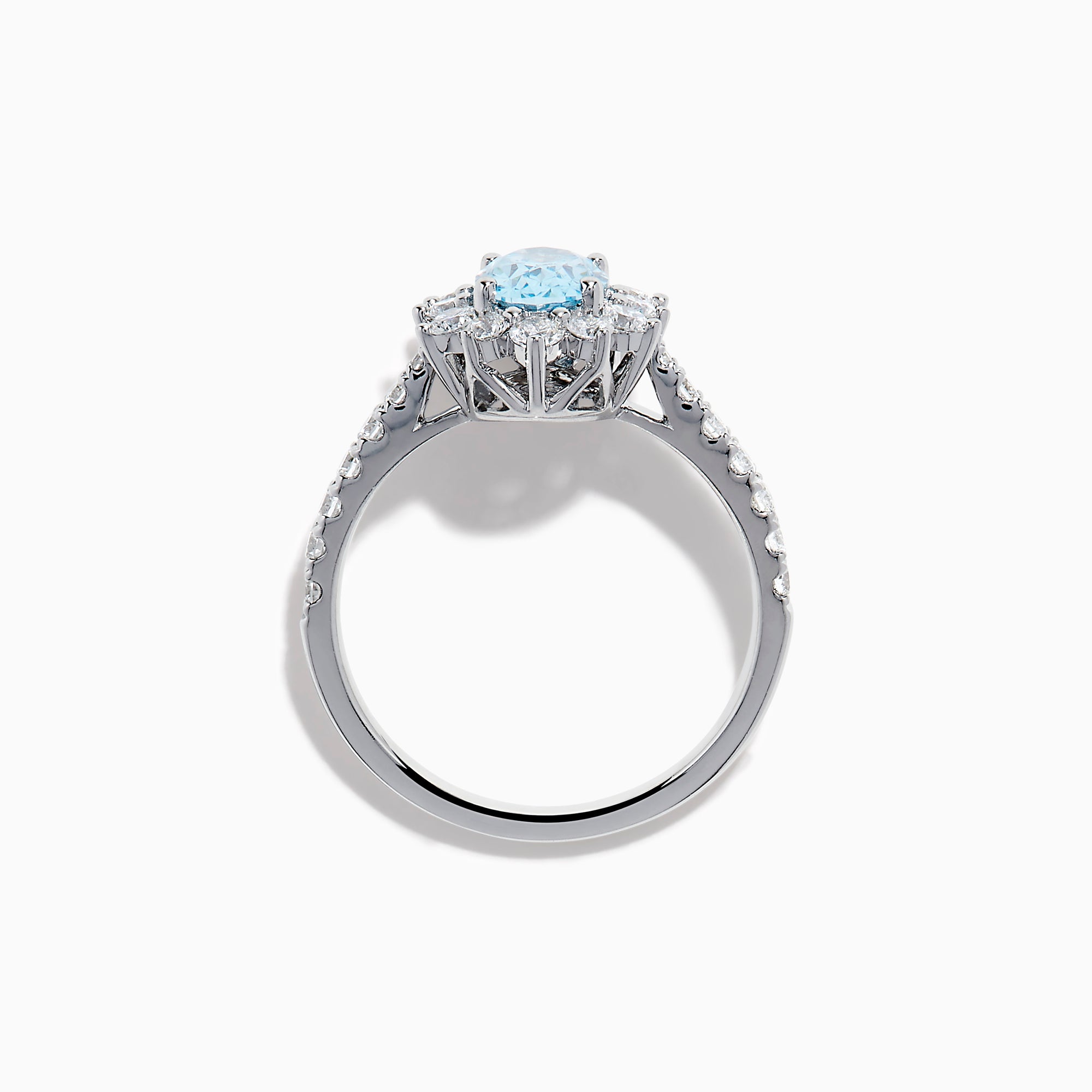 The Lab Grown Blue and White Diamond Halo Ring in 14K White Gold features an oval blue gemstone surrounded by lab grown diamonds, with more diamonds set along the band, shown on a white background.
