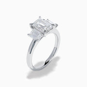 The Lab Grown Emerald Cut Diamond 3 Stone Ring in 14K White Gold features a central emerald-cut lab-grown diamond flanked by two rectangular diamonds on each side.