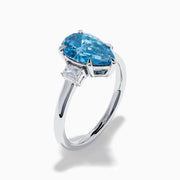 The Lab Grown Blue and White Diamond 3-Stone Ring in 14K White Gold features a large pear-shaped blue gemstone center with two rectangular lab grown diamonds, all set in white gold and displayed on a white background.