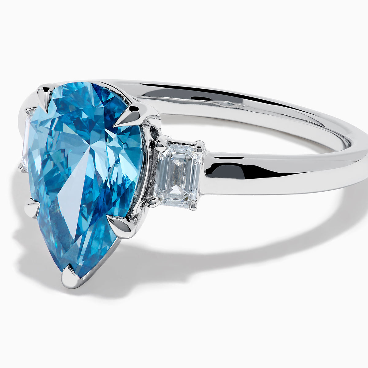 The Lab Grown Blue and White Diamond 3-Stone Ring in 14K White Gold features a large pear-shaped blue gemstone center with two rectangular lab grown diamonds, all set in white gold and displayed on a white background.