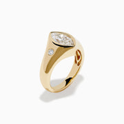 The Lab Grown Diamond Marquise Bezel Pinky Ring in 14K Yellow Gold features a central marquise lab grown diamond, accented by two small round diamonds on each side, all set on a sleek, polished band.