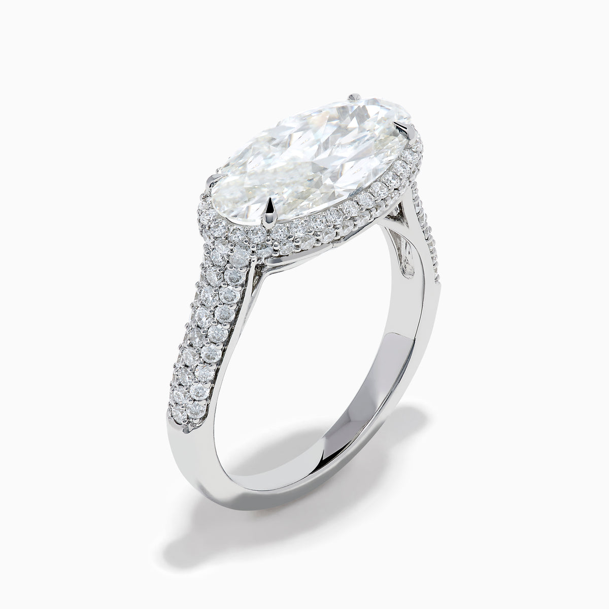 The Lab Grown Diamond East-West Oval Halo Ring in 14K White Gold showcases a brilliant lab-grown diamond center, accented by sparkling stones along the band, beautifully set against a plain white background.