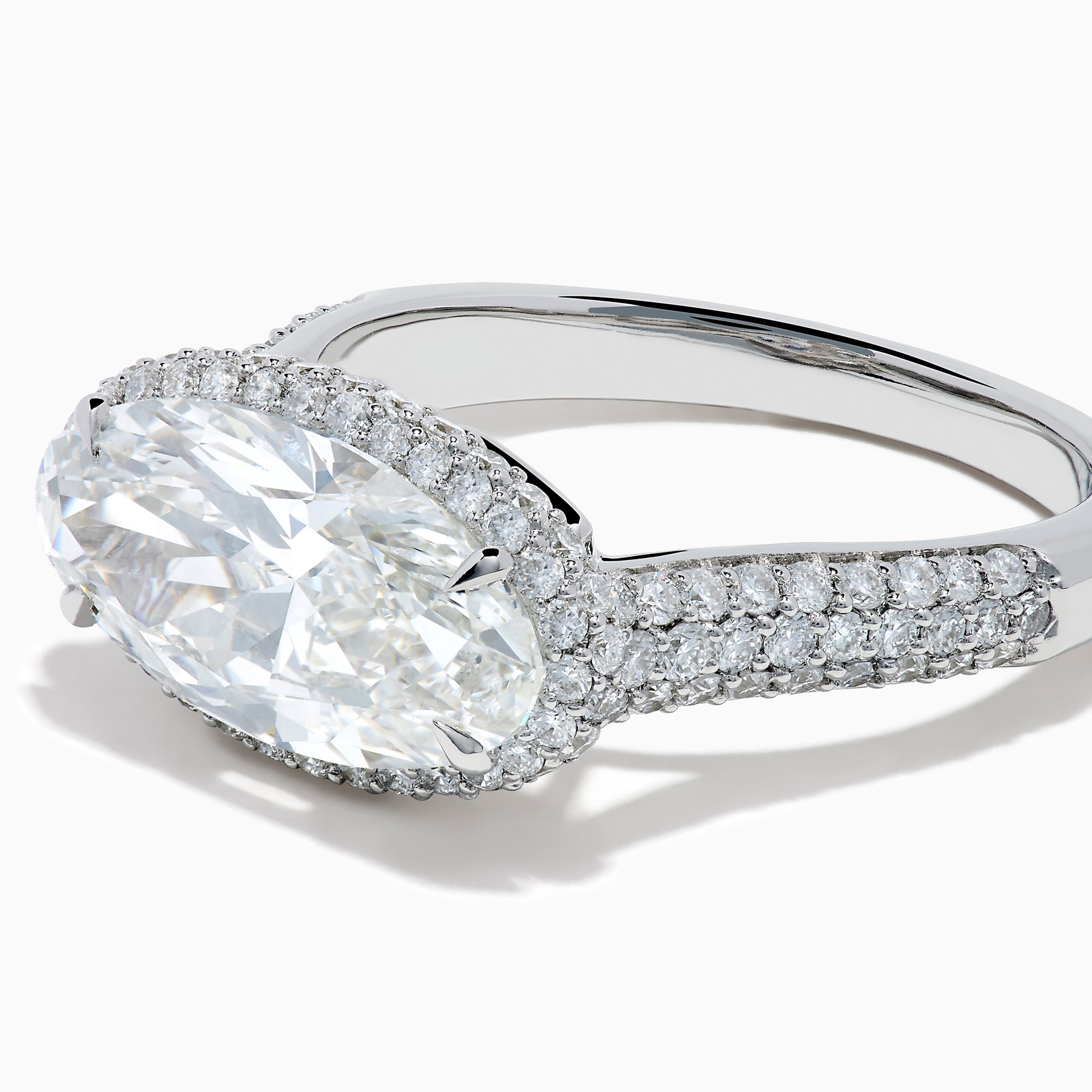 The Lab Grown Diamond East-West Oval Halo Ring in 14K White Gold showcases a brilliant lab-grown diamond center, accented by sparkling stones along the band, beautifully set against a plain white background.