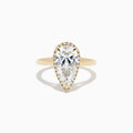The Lab Grown Elongated Pear Shaped Diamond Halo Ring in 14K Yellow Gold features a large pear-shaped lab-grown diamond surrounded by a halo of smaller round diamonds, displayed on a plain white background.