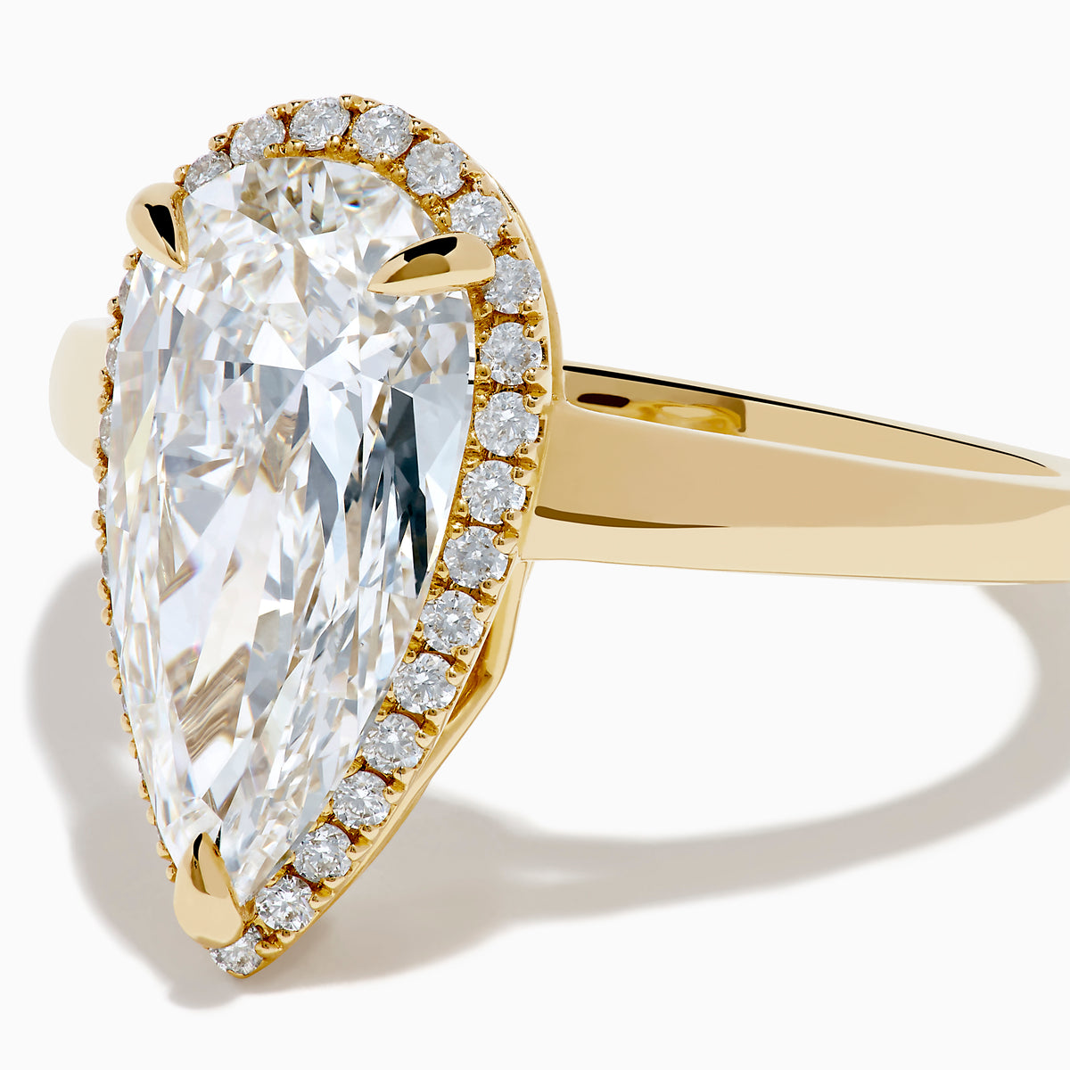 The Lab Grown Elongated Pear Shaped Diamond Halo Ring in 14K Yellow Gold features a large pear-shaped lab-grown diamond surrounded by a halo of smaller round diamonds, displayed on a plain white background.