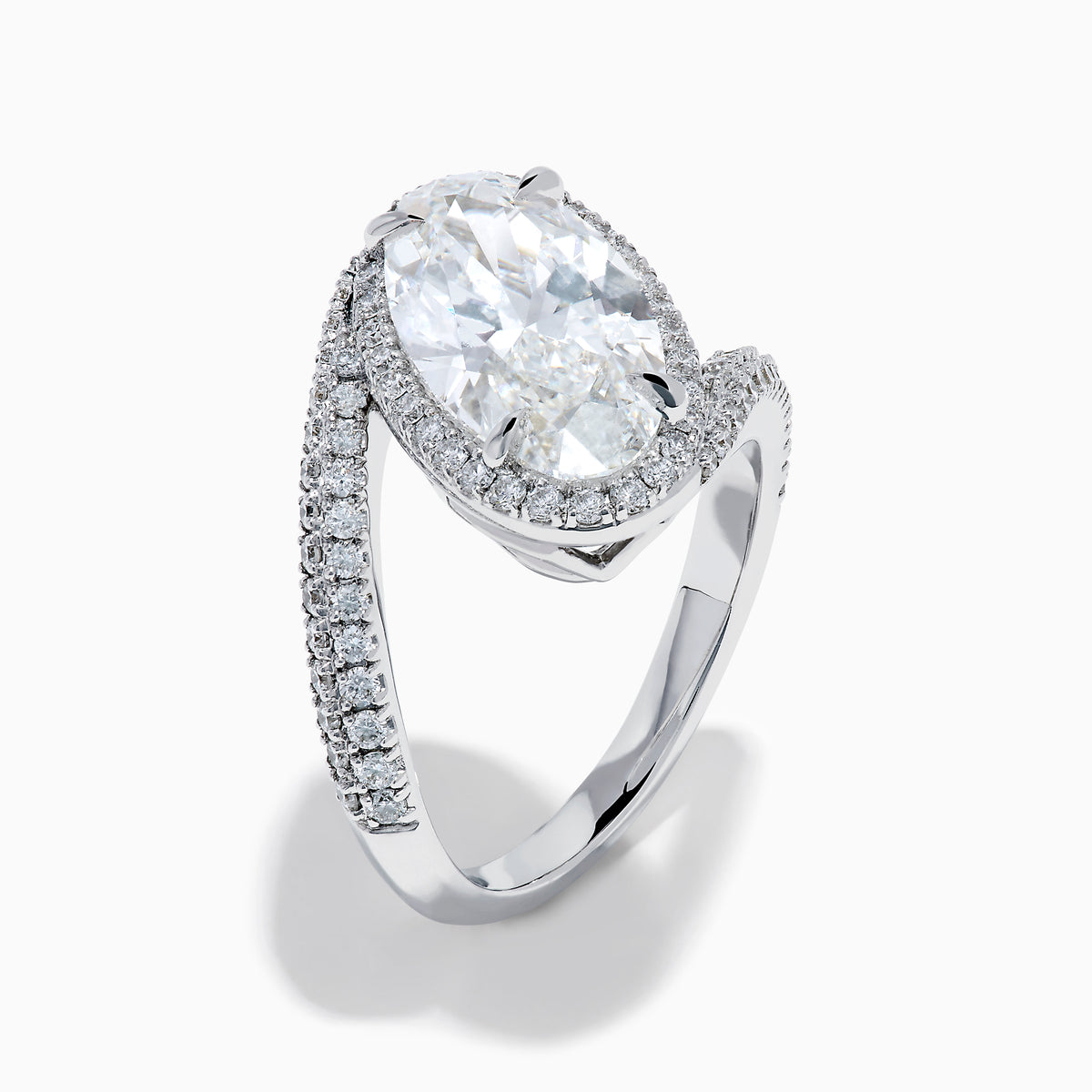 The Lab Grown Diamond Elongated Oval Halo Ring in 14K White Gold showcases a large oval lab diamond center, haloed by smaller diamonds with a diamond-adorned split shank, displayed on a clean white background.