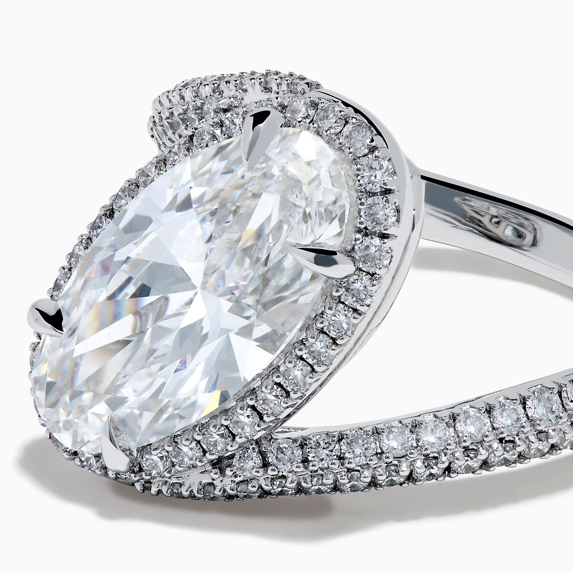 The Lab Grown Diamond Elongated Oval Halo Ring in 14K White Gold showcases a large oval lab diamond center, haloed by smaller diamonds with a diamond-adorned split shank, displayed on a clean white background.