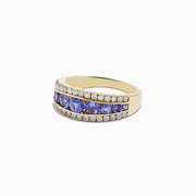 The Nahla Siri 14K Yellow Gold Tanzanite and Diamond Ring features a row of round blue tanzanite stones set between two rows of sparkling diamonds, shown on a white background.
