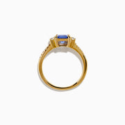 The 14K Yellow Gold Tanzanite and Diamond Ring showcases a square-cut blue tanzanite centerpiece, accented by round white diamonds set along the band.