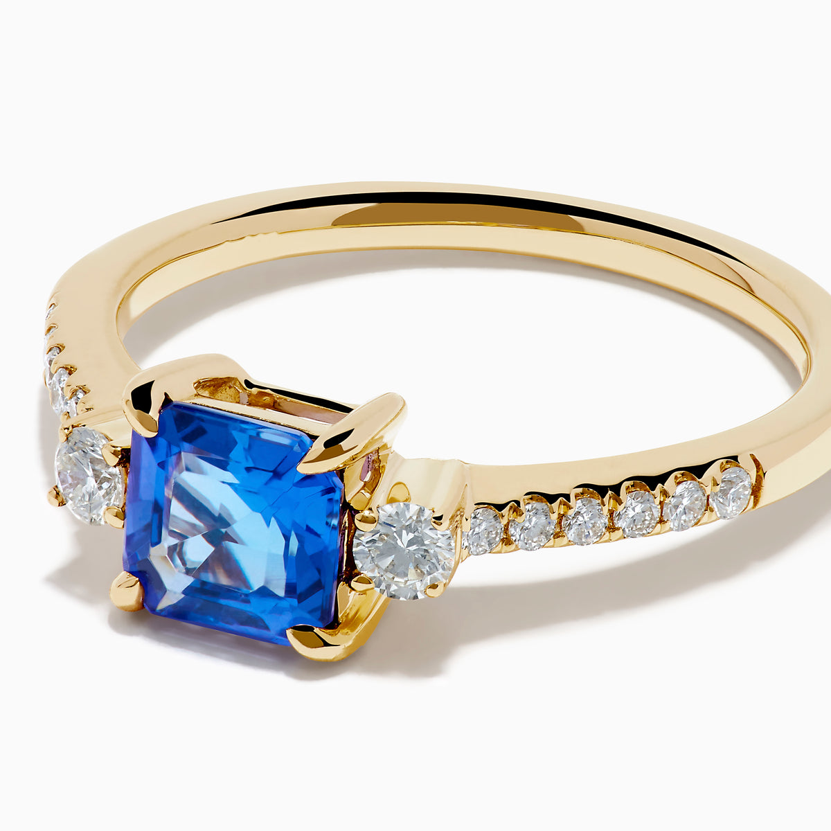 The 14K Yellow Gold Tanzanite and Diamond Ring showcases a square-cut blue tanzanite centerpiece, accented by round white diamonds set along the band.