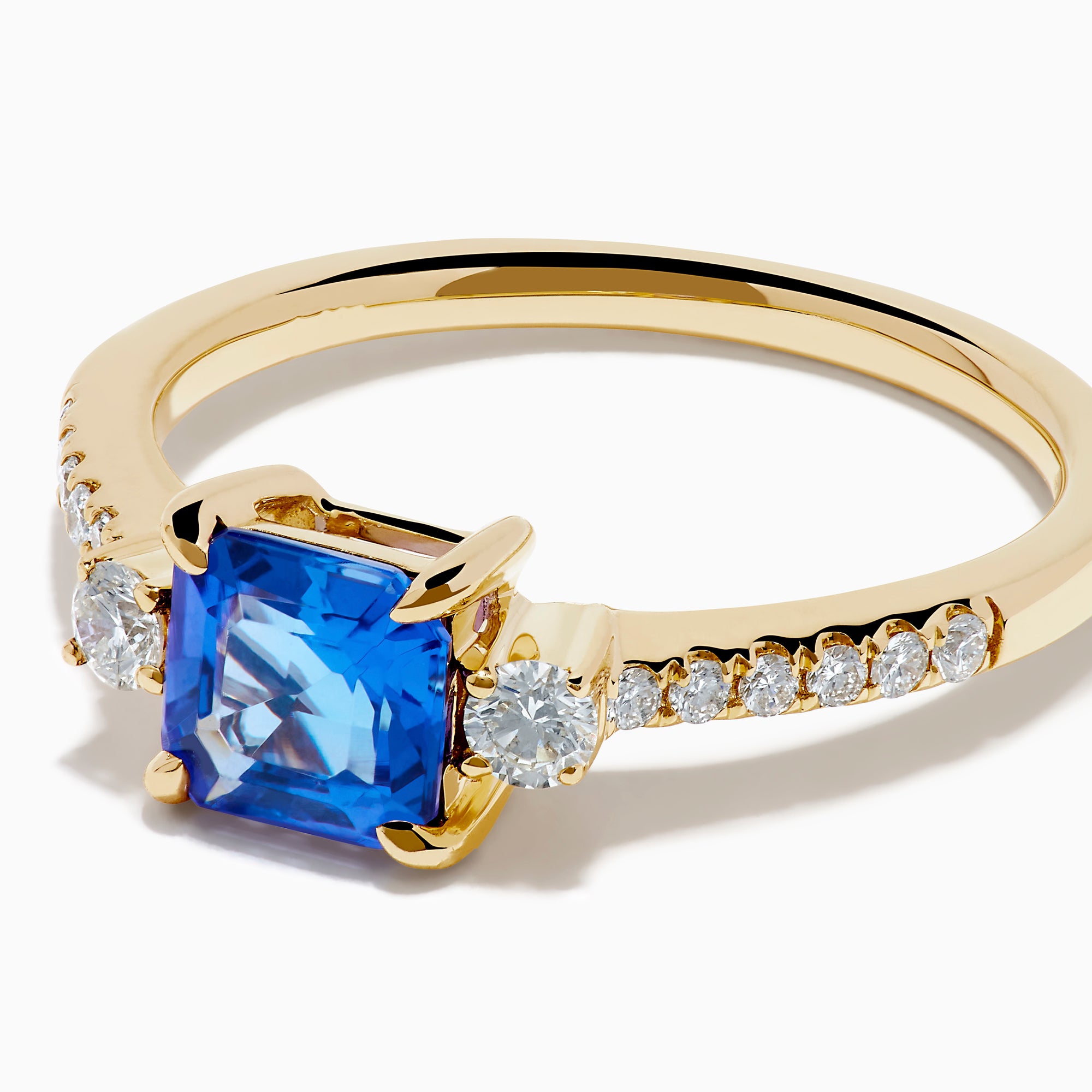 The 14K Yellow Gold Tanzanite and Diamond Ring showcases a square-cut blue tanzanite centerpiece, accented by round white diamonds set along the band.