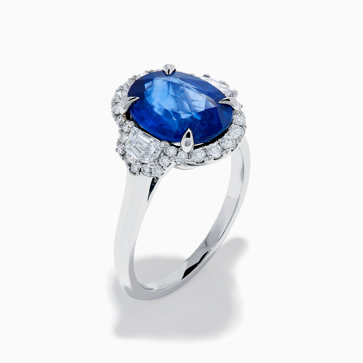 The Effy Hematian 18K White Gold Blue Sapphire and Diamond Halo Ring features a striking oval blue sapphire center, surrounded by round and rectangular diamonds, showcased on a plain white background.