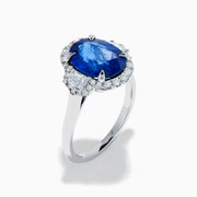 The Effy Hematian 18K White Gold Blue Sapphire and Diamond Halo Ring features a striking oval blue sapphire center, surrounded by round and rectangular diamonds, showcased on a plain white background.