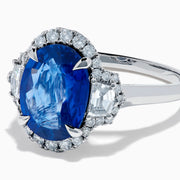 The Effy Hematian 18K White Gold Blue Sapphire and Diamond Halo Ring features a striking oval blue sapphire center, surrounded by round and rectangular diamonds, showcased on a plain white background.