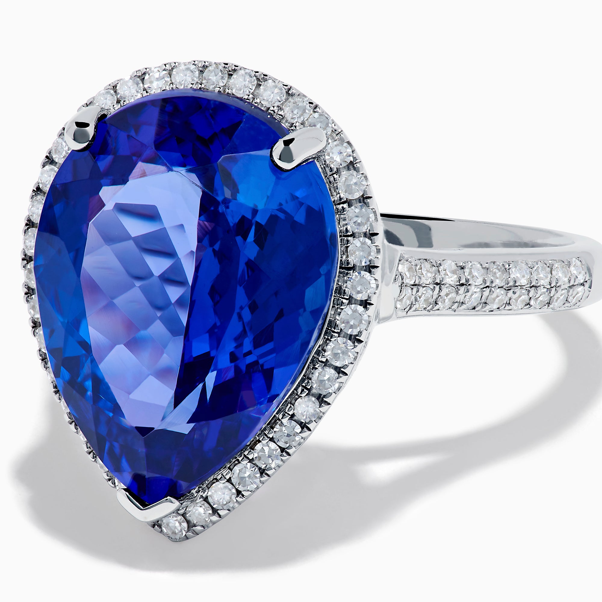 The 14K White Gold Pear Shape Tanzanite and Diamond Halo Ring features a pear-shaped blue tanzanite surrounded by a diamond halo on a delicate white gold band, displayed against a white background.