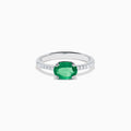 The 14K White Gold East West Oval Emerald and Diamond Ring showcases a striking green oval emerald set horizontally, accented by sparkling diamonds along the band.