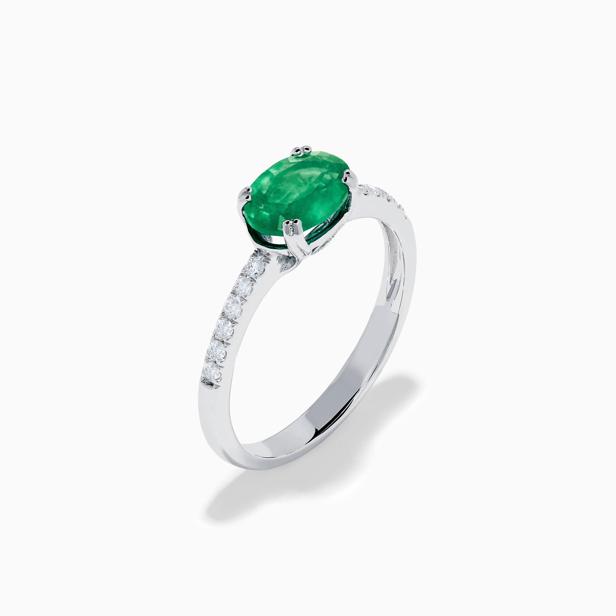 The 14K White Gold East West Oval Emerald and Diamond Ring showcases a striking green oval emerald set horizontally, accented by sparkling diamonds along the band.