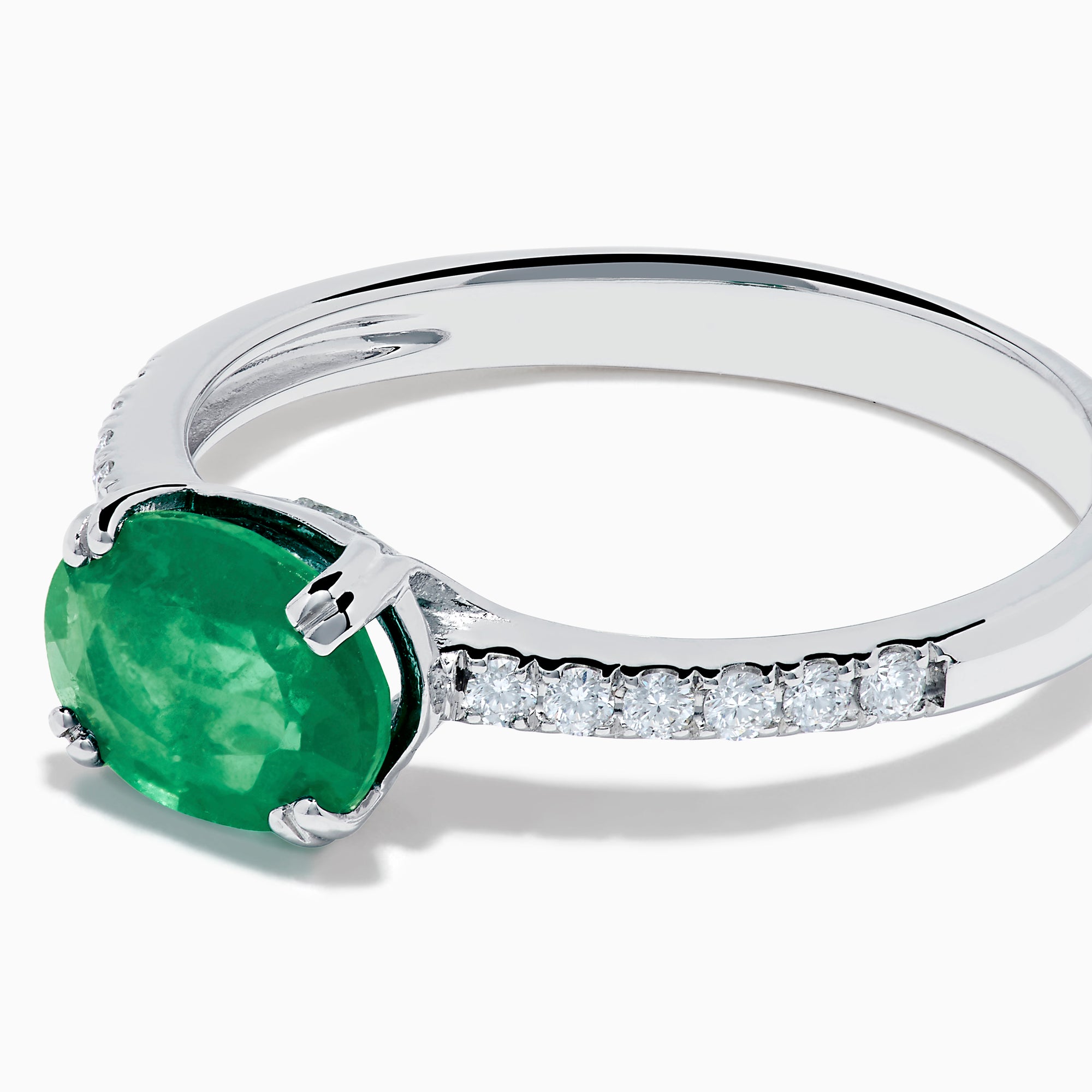 The 14K White Gold East West Oval Emerald and Diamond Ring showcases a striking green oval emerald set horizontally, accented by sparkling diamonds along the band.