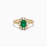 The Brasilica 14K Yellow Gold Emerald and Diamond Halo Ring features an emerald-cut green gemstone surrounded by a diamond halo, baguette-cut diamonds, and additional diamonds on the band.
