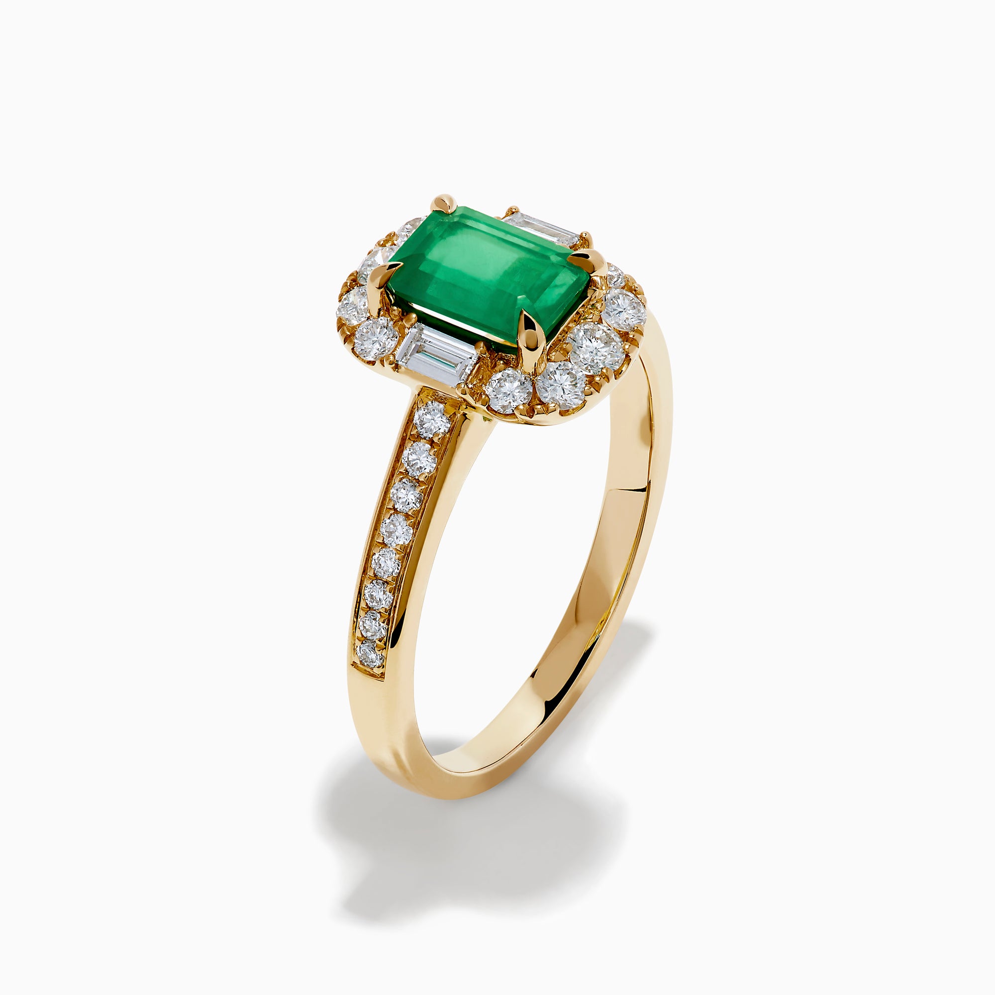The Brasilica 14K Yellow Gold Emerald and Diamond Halo Ring features an emerald-cut green gemstone surrounded by a diamond halo, baguette-cut diamonds, and additional diamonds on the band.