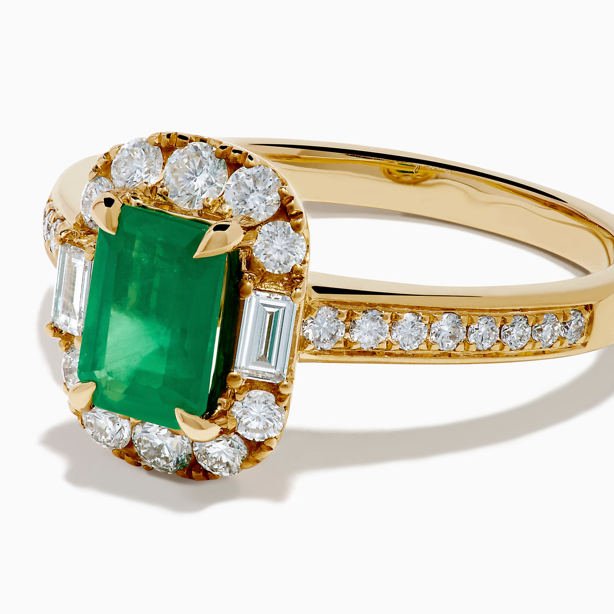 The Brasilica 14K Yellow Gold Emerald and Diamond Halo Ring features an emerald-cut green gemstone surrounded by a diamond halo, baguette-cut diamonds, and additional diamonds on the band.