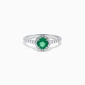 Introducing the 14K White Gold Emerald and Diamond Baguette Halo Ring, showcasing a round green emerald center stone, diamond baguette halo, and a band embellished with shimmering clear stones for added elegance.