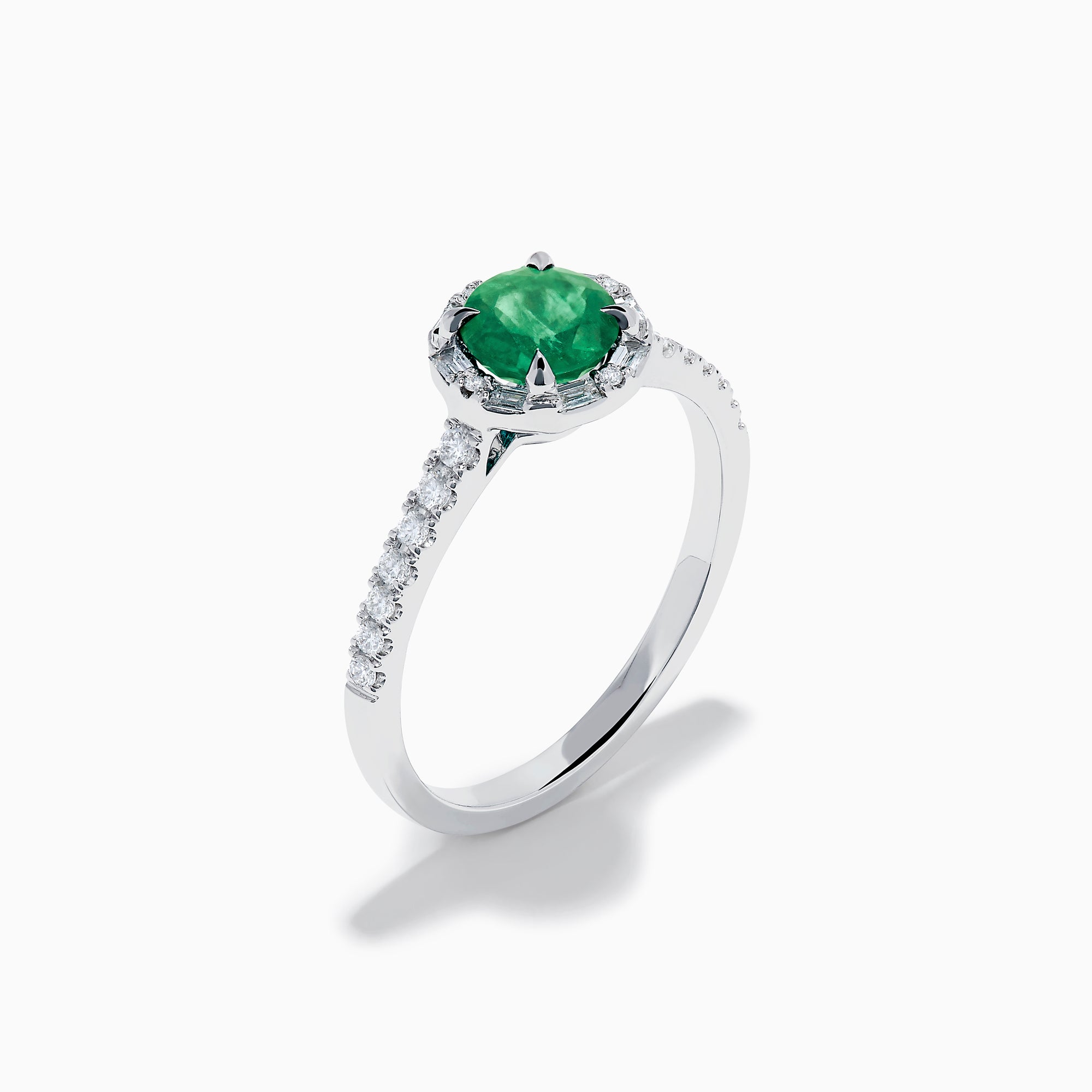 Introducing the 14K White Gold Emerald and Diamond Baguette Halo Ring, showcasing a round green emerald center stone, diamond baguette halo, and a band embellished with shimmering clear stones for added elegance.