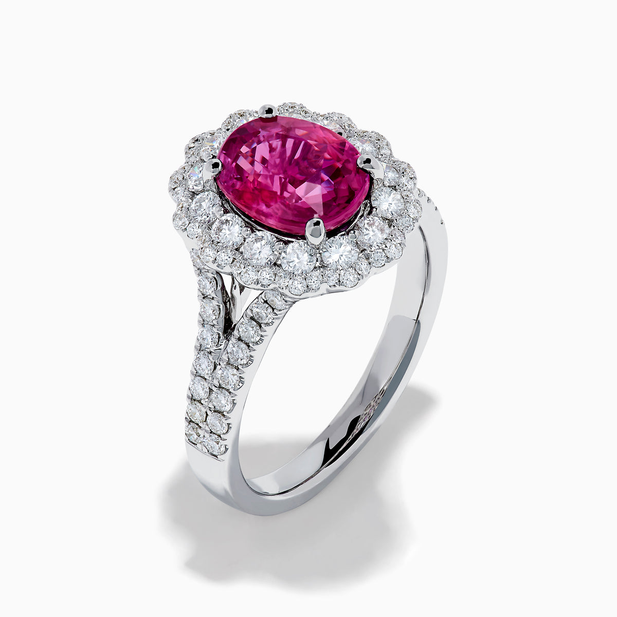 The 18K White Gold Pink Sapphire and Diamond Halo Ring features an oval pink sapphire surrounded by a diamond halo, with additional diamonds along the band for extra sparkle.