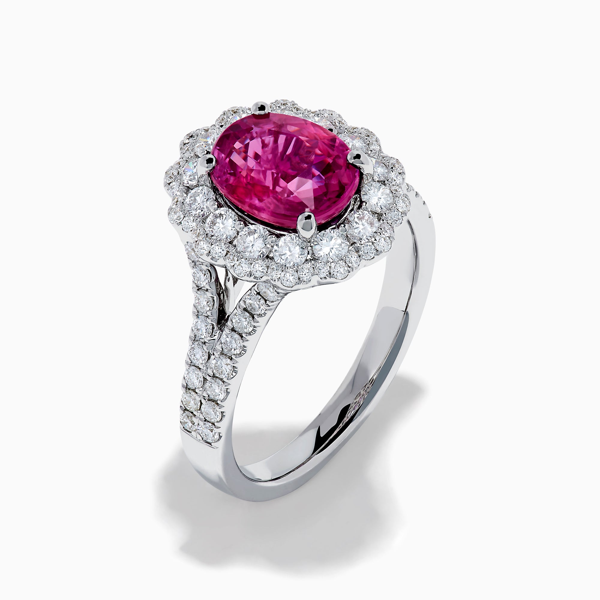 The 18K White Gold Pink Sapphire and Diamond Halo Ring features an oval pink sapphire surrounded by a diamond halo, with additional diamonds along the band for extra sparkle.