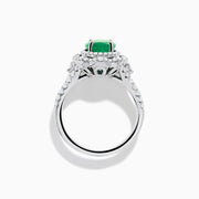The 18K White Gold Emerald and Diamond Ring features an oval green emerald center stone, two diamond halos, and sparkling diamonds set along the band.