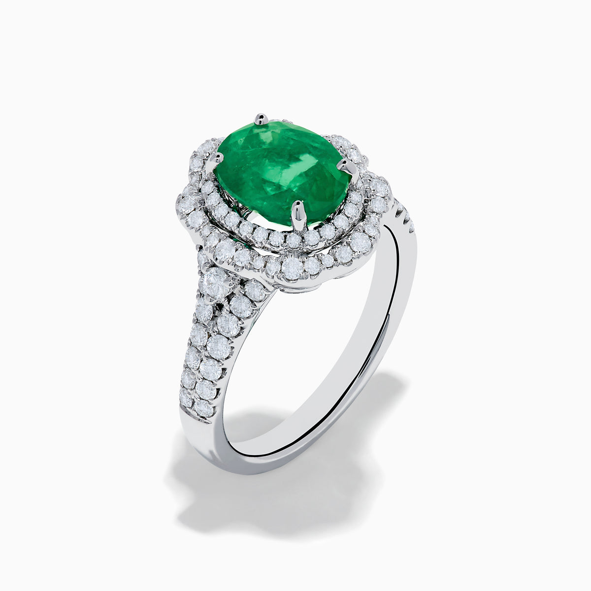 The 18K White Gold Emerald and Diamond Ring features an oval green emerald center stone, two diamond halos, and sparkling diamonds set along the band.