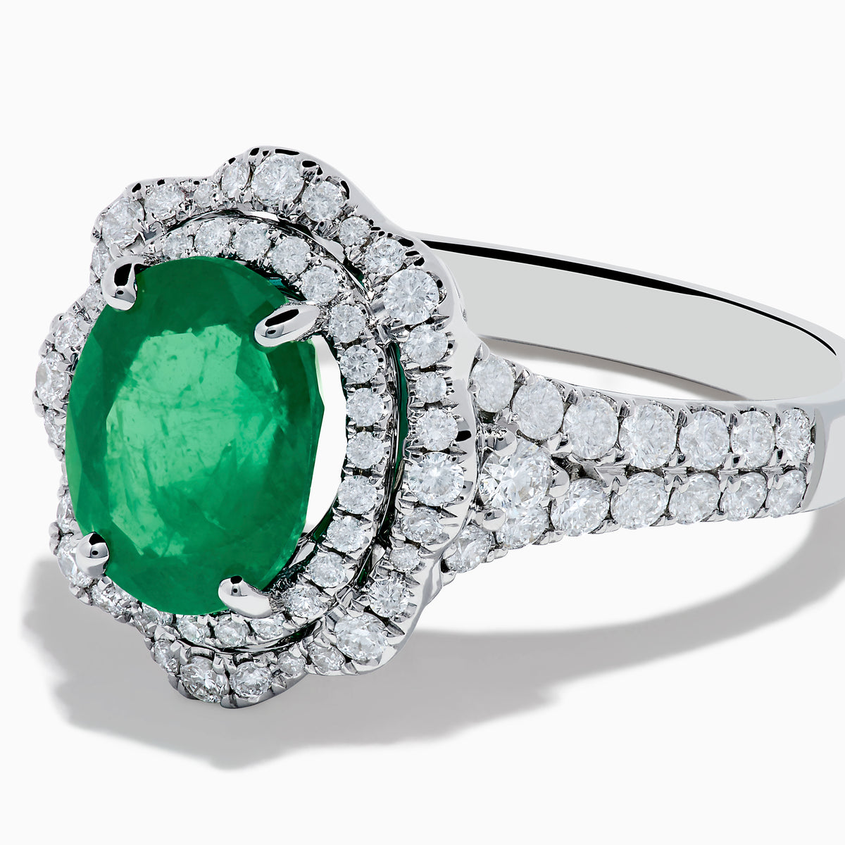 The 18K White Gold Emerald and Diamond Ring features an oval green emerald center stone, two diamond halos, and sparkling diamonds set along the band.