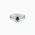 The 14K White Gold White and Black Diamond Halo Ring features an oval black center stone, a halo of white diamonds, and additional diamonds set along its split shank band.