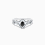 The 14K White Gold White and Black Diamond Halo Ring features an oval black center stone, a halo of white diamonds, and additional diamonds set along its split shank band.