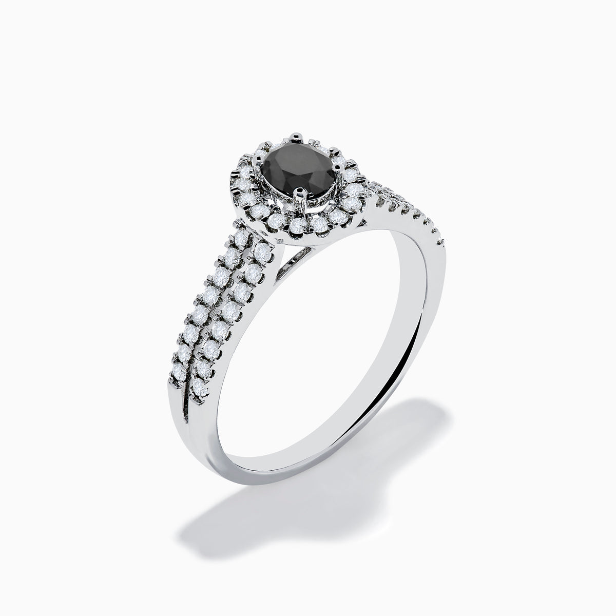 The 14K White Gold White and Black Diamond Halo Ring features an oval black center stone, a halo of white diamonds, and additional diamonds set along its split shank band.