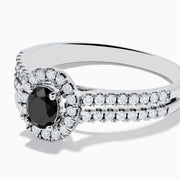 The 14K White Gold White and Black Diamond Halo Ring features an oval black center stone, a halo of white diamonds, and additional diamonds set along its split shank band.