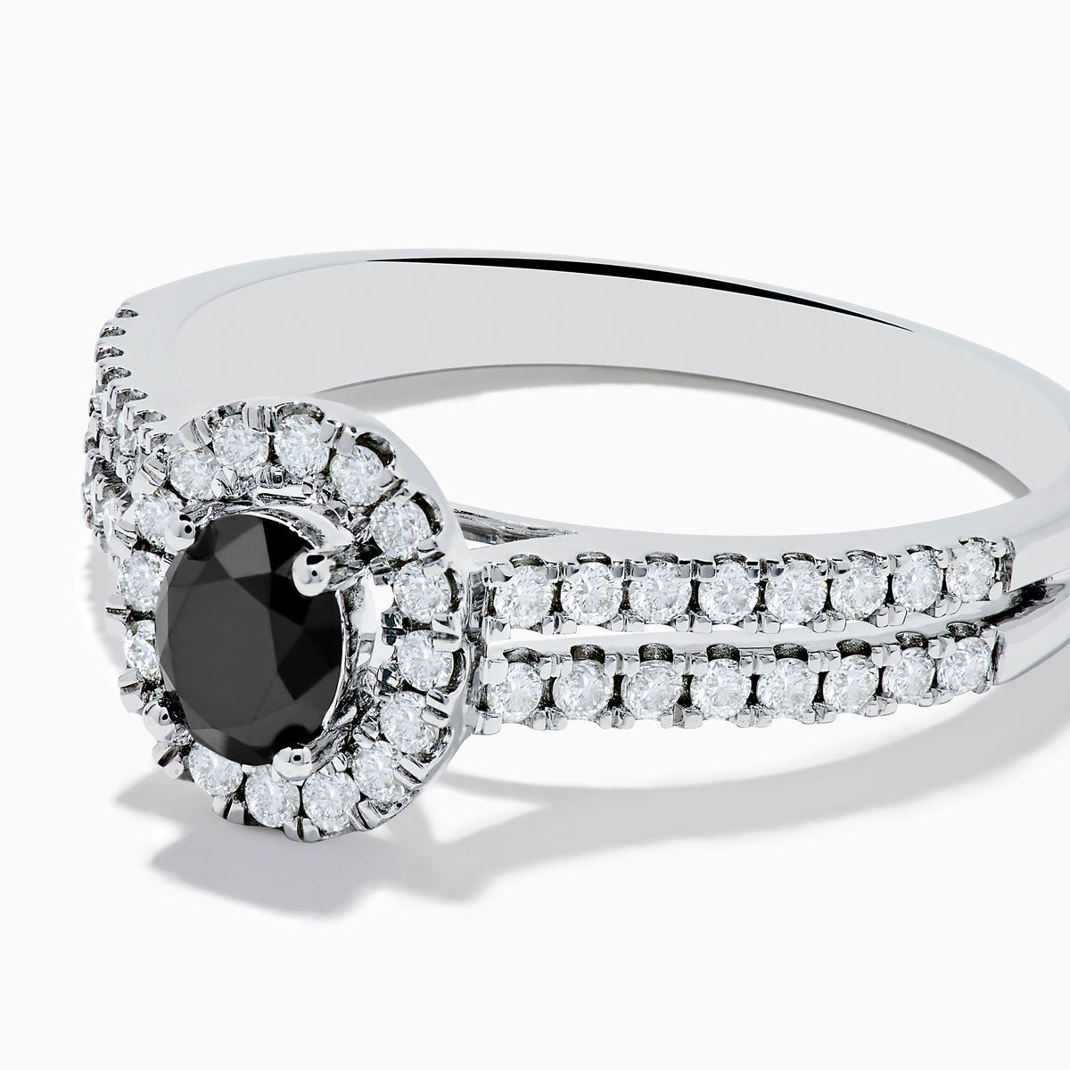 The 14K White Gold White and Black Diamond Halo Ring features an oval black center stone, a halo of white diamonds, and additional diamonds set along its split shank band.