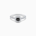 The 14K White Gold White and Black Diamond Halo Ring features a rectangular black center stone surrounded by white diamonds, with more diamonds along the band, all presented on a white background.