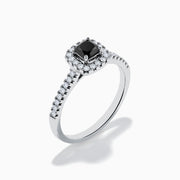 The 14K White Gold White and Black Diamond Halo Ring features a rectangular black center stone surrounded by white diamonds, with more diamonds along the band, all presented on a white background.