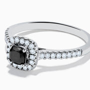 The 14K White Gold White and Black Diamond Halo Ring features a rectangular black center stone surrounded by white diamonds, with more diamonds along the band, all presented on a white background.