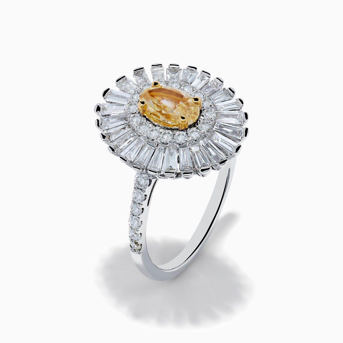 The Canare 18K Two Tone Gold Yellow and White Diamond Ring features an oval yellow centerpiece with a starburst halo of round and baguette white diamonds on a slim, diamond-studded band.