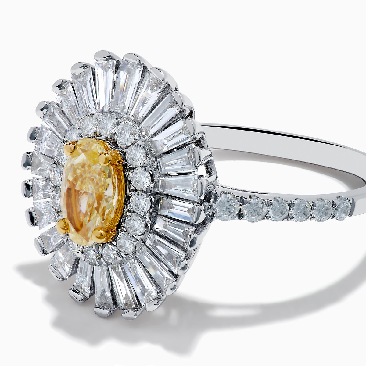 The Canare 18K Two Tone Gold Yellow and White Diamond Ring features an oval yellow centerpiece with a starburst halo of round and baguette white diamonds on a slim, diamond-studded band.