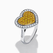 The Canare 18K Two Tone Gold Yellow Diamond Heart Ring, featuring a yellow diamond center with clear white stones on a silver band, is displayed against a white background.