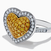 The Canare 18K Two Tone Gold Yellow Diamond Heart Ring, featuring a yellow diamond center with clear white stones on a silver band, is displayed against a white background.