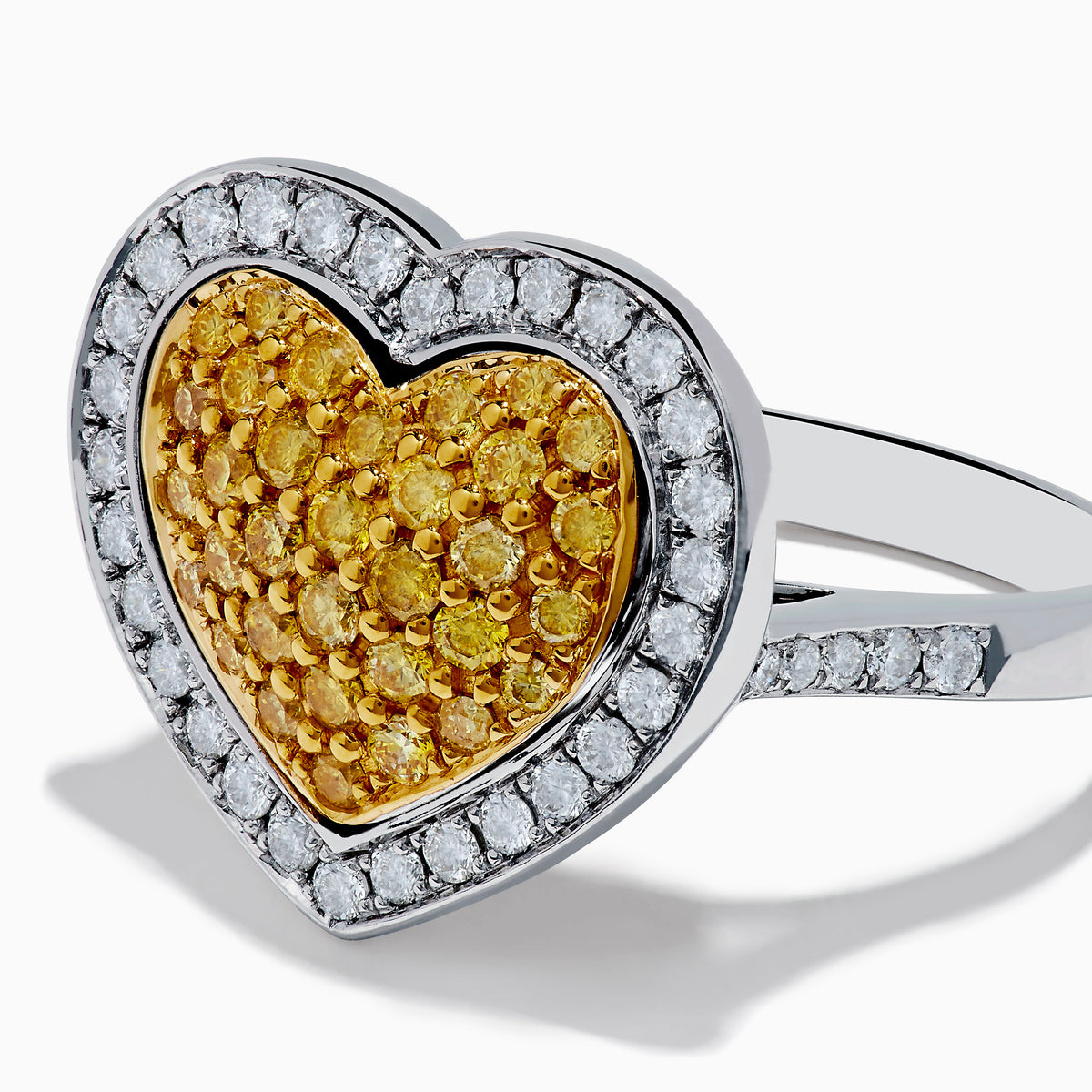 The Canare 18K Two Tone Gold Yellow Diamond Heart Ring, featuring a yellow diamond center with clear white stones on a silver band, is displayed against a white background.
