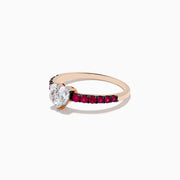 The 14k Rose Gold Ruby and Diamond Heart Ring features a heart-shaped diamond center and a band adorned with small rubies, showcased from the front on a white background.